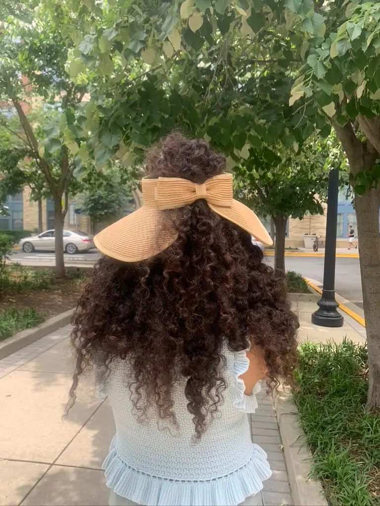 woman with curly hair wearing woven sunvisor outside