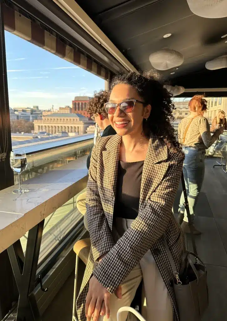Woman in Avec Les Filles Coat smiling on a rooftop balcony