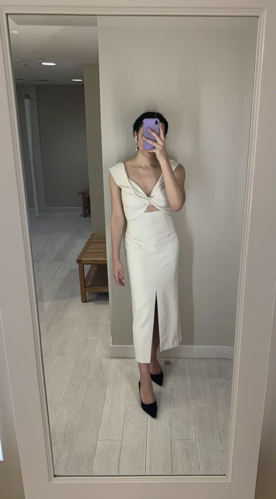 Woman in mirror wearing a cream colored midi dress Nuuly rental and black heels.