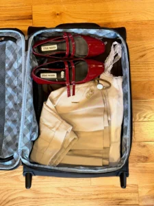 suitcase of clothing featuring red flats and neutral trousers for a trip