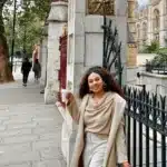 woman in monochrome neutral outfit with cowl neck sweater, trench coat, and tan trousers