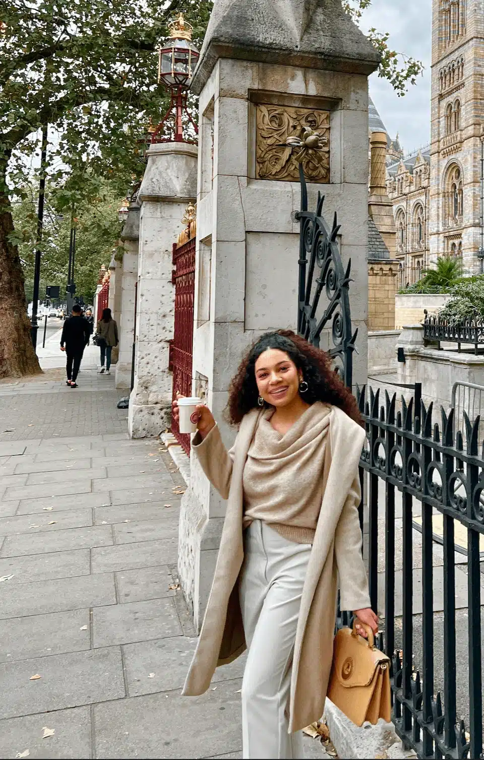 woman in monochrome neutral outfit with cowl neck sweater, trench coat, and tan trousers