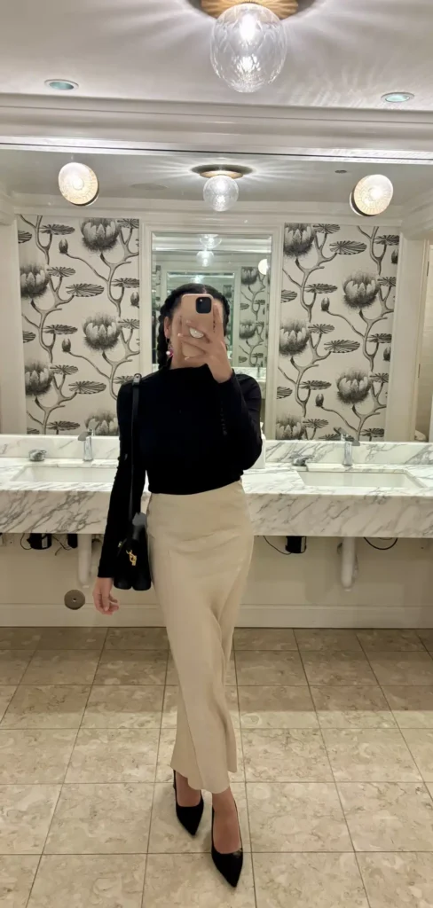 woman in elegant Quince silk skirt and black turtleneck with black leather shoulder bag