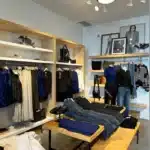 Store with denim folded on wood tables and blazers hanging in the back