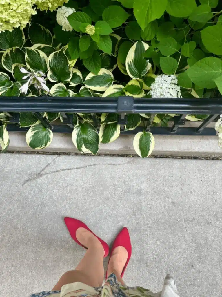 woman in red pointed toe flats on sidewalk with flowers