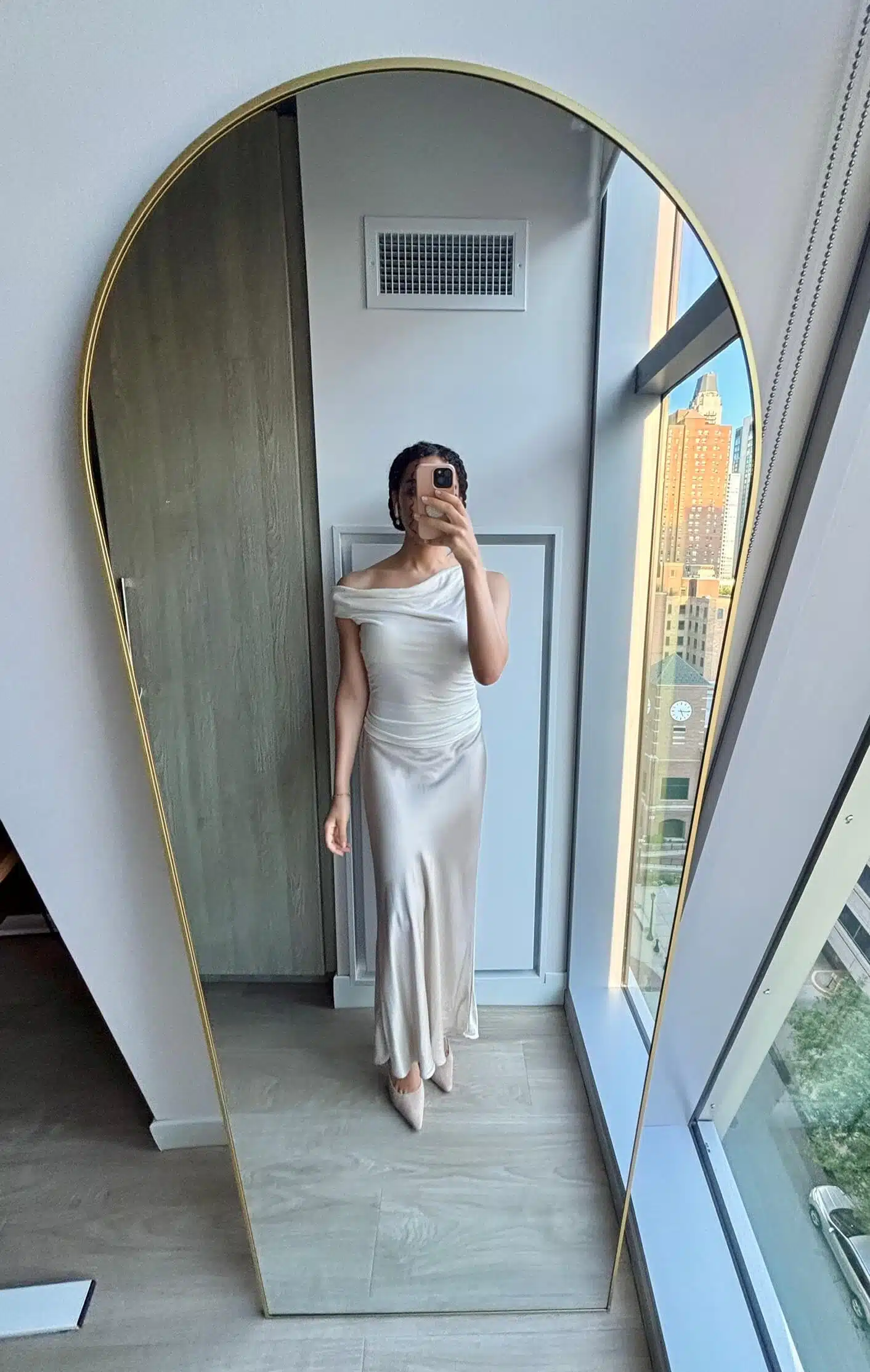 Woman wearing a champagne Quince silk maxi skirt with a cream off-the-shoulder top in a mirror selfie
