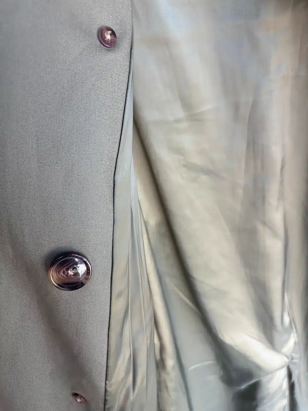 Quince trench front edge showing its polyester lining and a four-hole cross-stitched button