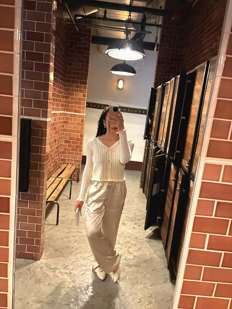 Woman wearing champagne Quince washable silk drawstring wide-leg pants with a cream knit cardigan