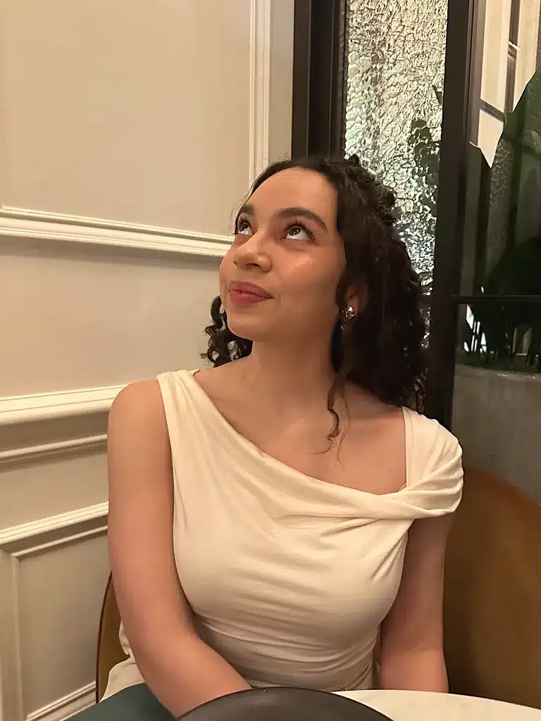 Woman wearing a cream Reformation Cello top with a twisted one-shoulder drape, made of Tencel lyocell with spandex