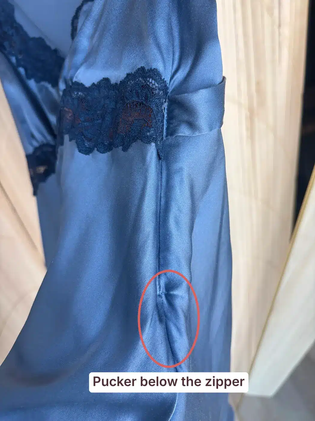 Side seam of a blue Reformation silk dress with a pucker circled below the zipper